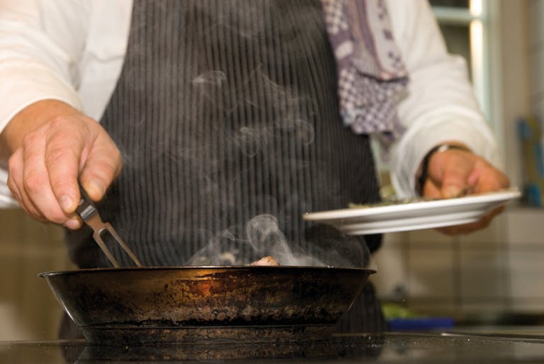 A chef skillfully prepares a dish in a professional kitchen, surrounded by smoke.